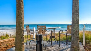 Eine Terrassensitzgelegenheit am Strand mit Tisch und Stühlen, mit Blick auf den Ozean.