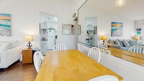 Ein Zimmer mit Esstisch aus Holz, weißen Stühlen, einem weißen Sofa und einem großen Spiegel, der den Raum widerspiegelt.