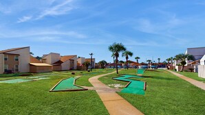 Ein Golfplatz mit gepflegtem Weg, Palmen und einem Gebäude im Hintergrund.