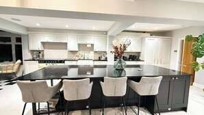 A modern kitchen with white cabinets, a large black island, and three grey chairs. - Dreamy Stay With Cosy Charm (Addlestone)