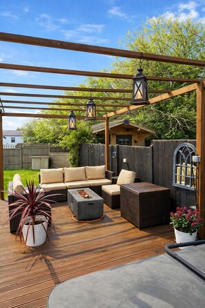 Patio esterno coperto con una pergola in legno, sedute imbottite e lanterne sospese.
