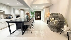 A modern kitchen with a central island, a dining area with a round wicker sofa, and a potted plant. - Dreamy Stay With Cosy Charm (Addlestone)