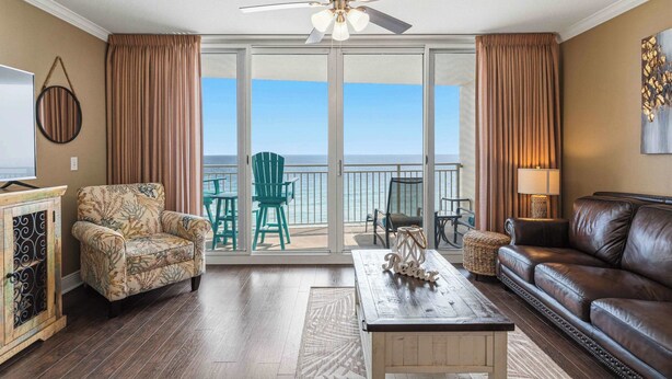 Ein Wohnzimmer mit einer Couch, einem Sessel und einem Couchtisch, einem Deckenventilator und Blick auf das Meer durch große Schiebetüren.
