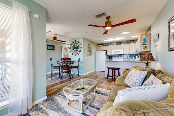 A living room with a glass coffee table, a sofa, and a dining area with chairs and a table.