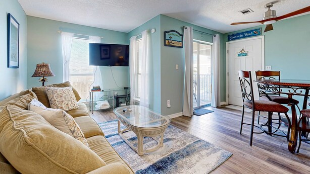 A living room with a sofa, coffee table, and dining table with chairs. There is a television, a lamp, and a sign that says "Gone to the Beach". - Bayview condo only steps from the beach w/ shared pool and peaceful location (Navarre Beach)