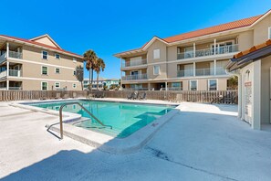 A hotel with a swimming pool, multiple balconies, and a fenced deck area.
