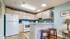 A kitchen with a central island, wooden cabinets, a microwave, and a refrigerator. - Bayview condo only steps from the beach w/ shared pool and peaceful location (Navarre Beach)