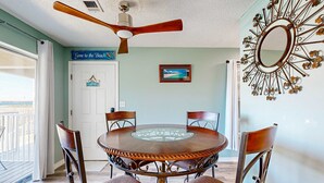 A dining area with a round table, four chairs, a ceiling fan, a decorative mirror, and a door with a 'Gone to the Beach' sign. - Bayview condo only steps from the beach w/ shared pool and peaceful location (Navarre Beach)