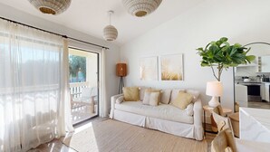 Una sala de estar moderna con un sofá, una planta grande y una cocina al fondo.