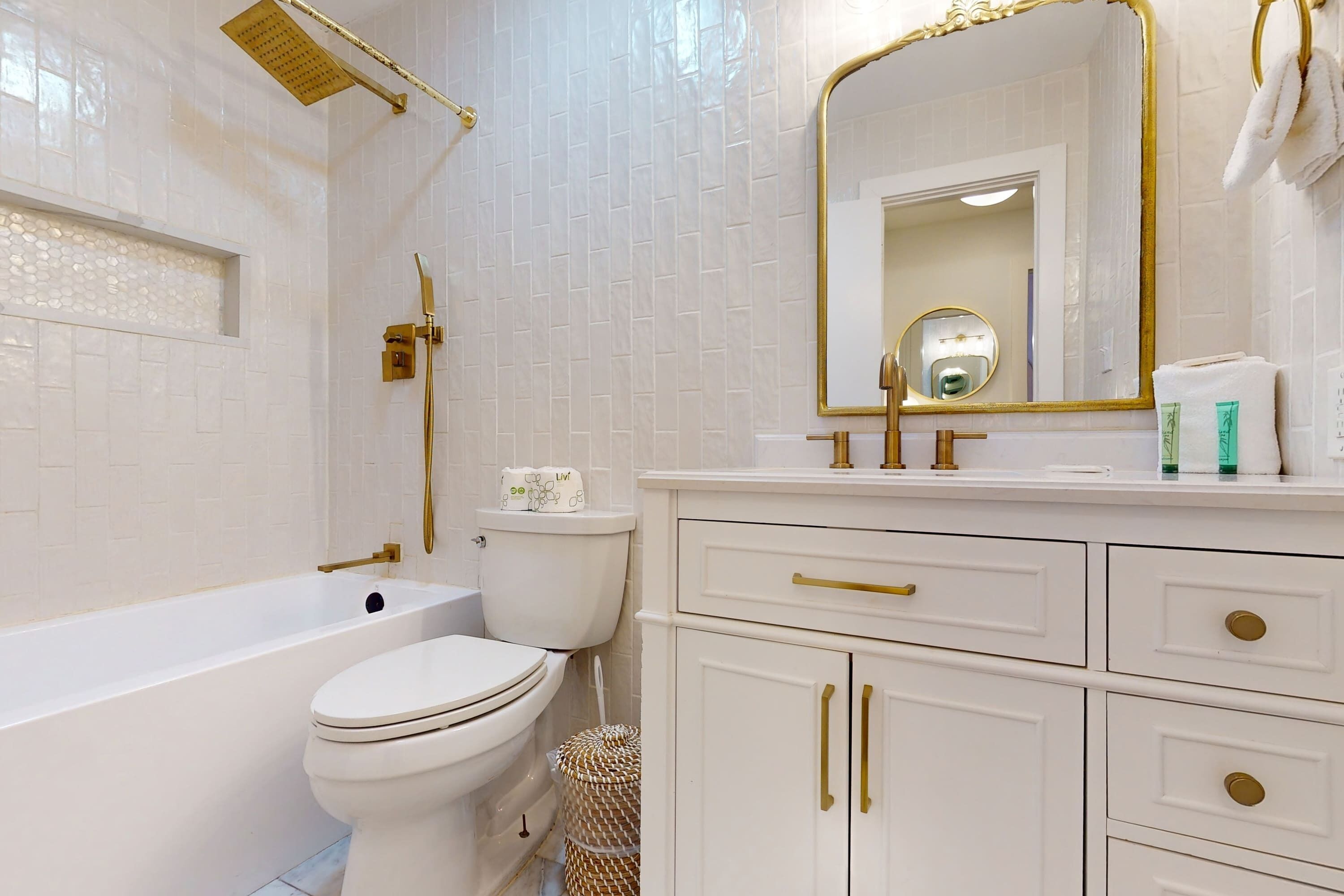 A bathroom with a white bathtub, toilet, and vanity with gold handles.