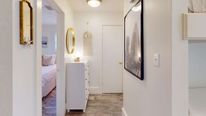 Un pasillo con un aparador blanco, un cuadro en la pared y una puerta al final.