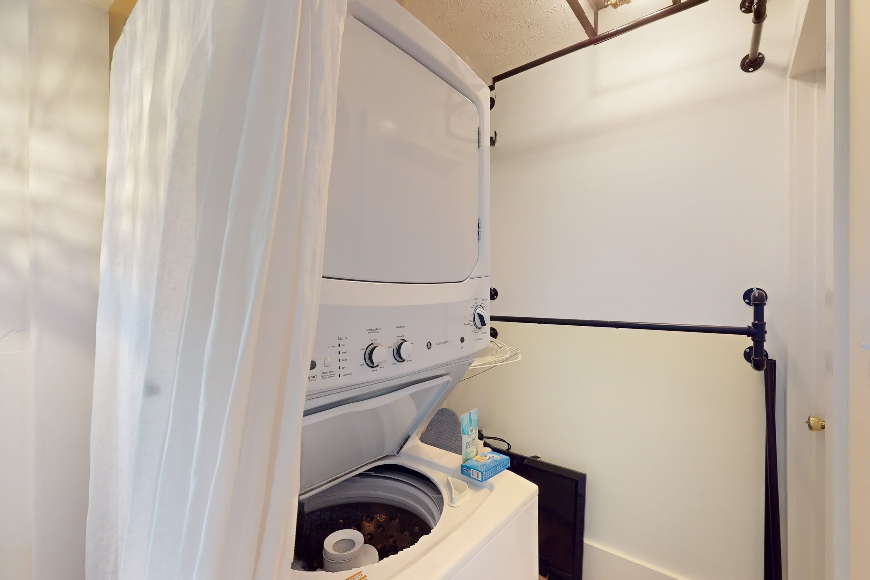 Une petite buanderie équipée d’un lave-linge et d’un sèche-linge à chargement frontal, d’un porte-serviettes et d’une porte dotée d’une poignée noire.