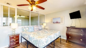 A bedroom with a bed, a nightstand, a dresser, a ceiling fan, a TV mounted on the wall, and a window with blinds. - Cozy condo with pools, tennis, gym, mini golf, beach access, & balcony (Panama City Beach)