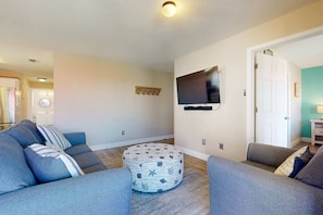 A living room with a sectional sofa, ottoman, and a flat-screen TV mounted on the wall.