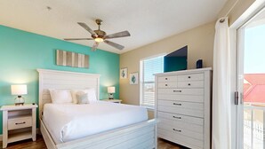 Un dormitorio con una cama blanca, ventilador de techo, cómoda y ventana con persianas.