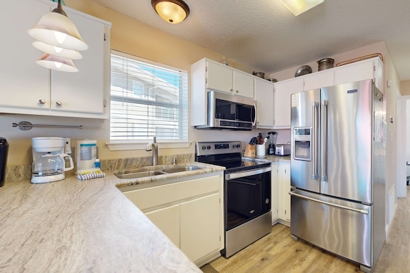 A modern kitchen with white cabinets, stainless steel appliances, a built-in oven, and a large refrigerator.