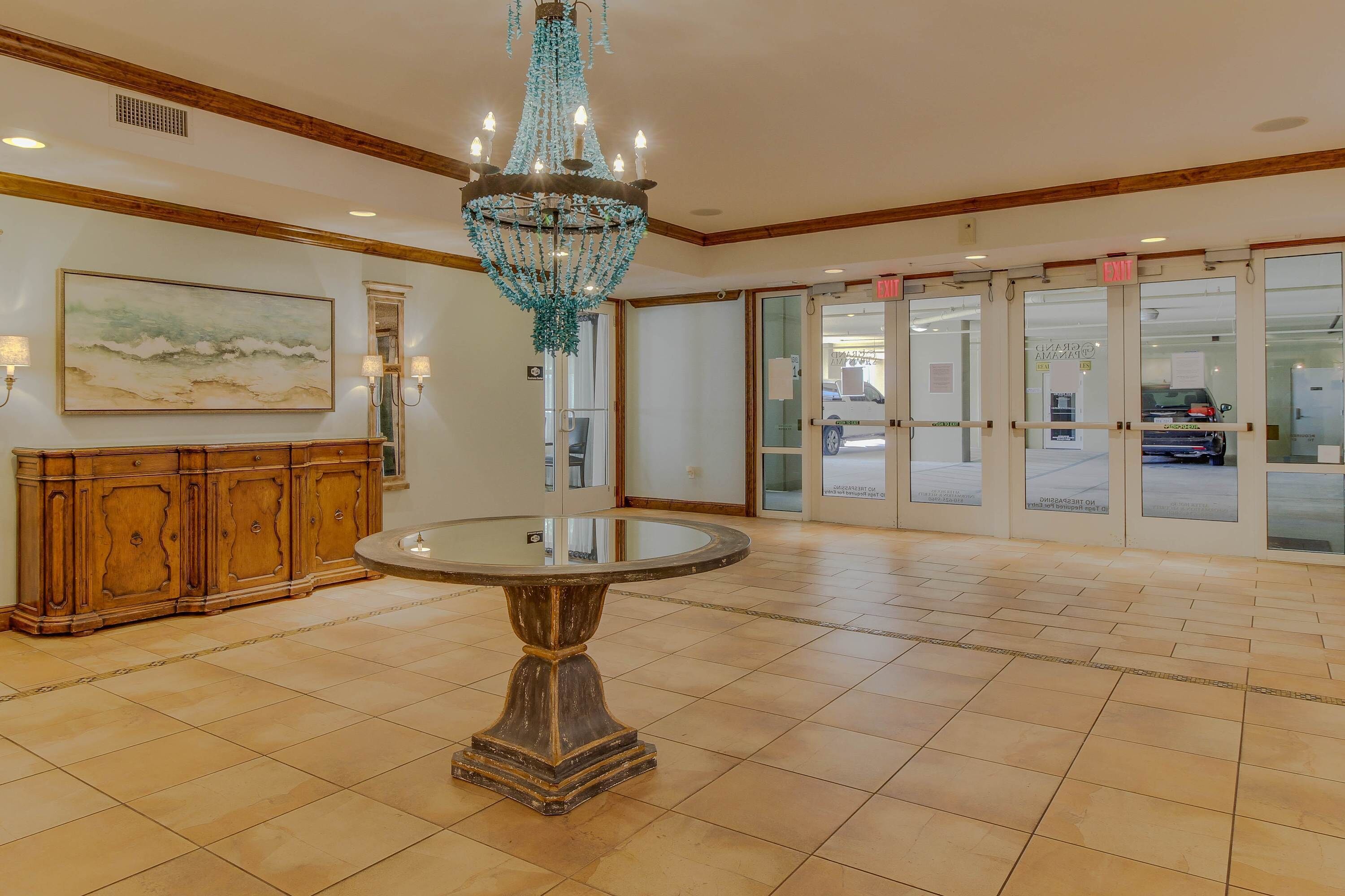 Un hall d’entrée avec un lustre, une table ronde, un meuble en bois et un tableau accroché au mur.