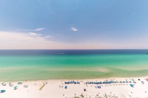 A beach with clear turquoise water, a sandy shore, and rows of blue umbrellas. - Lovely coastal condo with water views, pool, hot tub, private balcony & W/D (Panama City Beach)