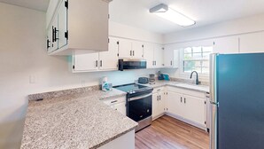 Una cucina moderna con mobili bianchi, ripiani in granito, frigorifero in acciaio inossidabile e forno a microonde integrato.