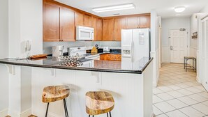 Eine moderne Küche mit Holzschränken, einer zentralen Kochinsel mit Hockern und einem Kühlschrank.