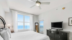 Ein Schlafzimmer mit Bett, Fernseher, Kommode und einem Fenster mit Meerblick.