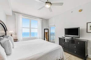 A bedroom with a bed, a TV, a dresser, and a window with a view of the sea. - Renovated oceanfront condo with pools, hot tub & AC (Panama City Beach)
