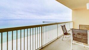 Een balkon met uitzicht op de oceaan en een pier. Er staat een stoel en een klein tafeltje.