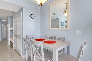 A dining area with a white table and chairs, a clock on the wall, and a mirror reflecting the room. - Sunny oceanfront condo w/ two shared pools, hot tub - walk to the beach (Panama City Beach)