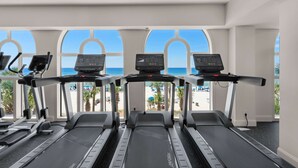 A gym with treadmills and exercise equipment, large windows with a view of a beach and palm trees. - Beach-view, high-rise condo with pool - central location (Panama City Beach)
