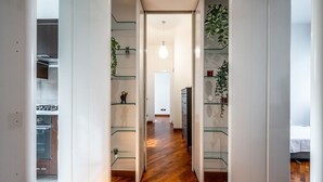Un estrecho pasillo con estantes de vidrio a cada lado, que conduce a una zona de cocina con estufa y armarios.