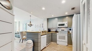 A modern kitchen with grey cabinets, a white refrigerator, and a microwave. - Stylish oceanfront condo including shared pool and beach access (Panama City Beach)