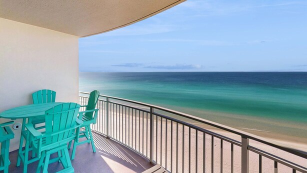 A balcony with a view of the ocean, a table, and green chairs. - Stylish oceanfront condo including shared pool and beach access (Panama City Beach)