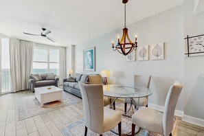 Ein modernes Wohnzimmer mit einem Glastisch, grau gepolsterten Stühlen, einem weißen Couchtisch und einem Deckenventilator.