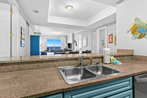 A modern kitchen with granite countertops, stainless steel sinks, and teal cabinetry. - All-suite condo with Gulf views, beach access, balcony, pool, spa, gym, & AC (Panama City Beach)