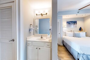 Una camera d'albergo con una toeletta bianca, uno specchio grande, un comodino, un letto con copripiumino blu e un quadro sopra il letto.