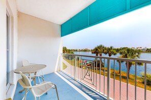Un balcone con tavolo e sedie, affacciato su uno specchio d'acqua con palme e un edificio in lontananza.