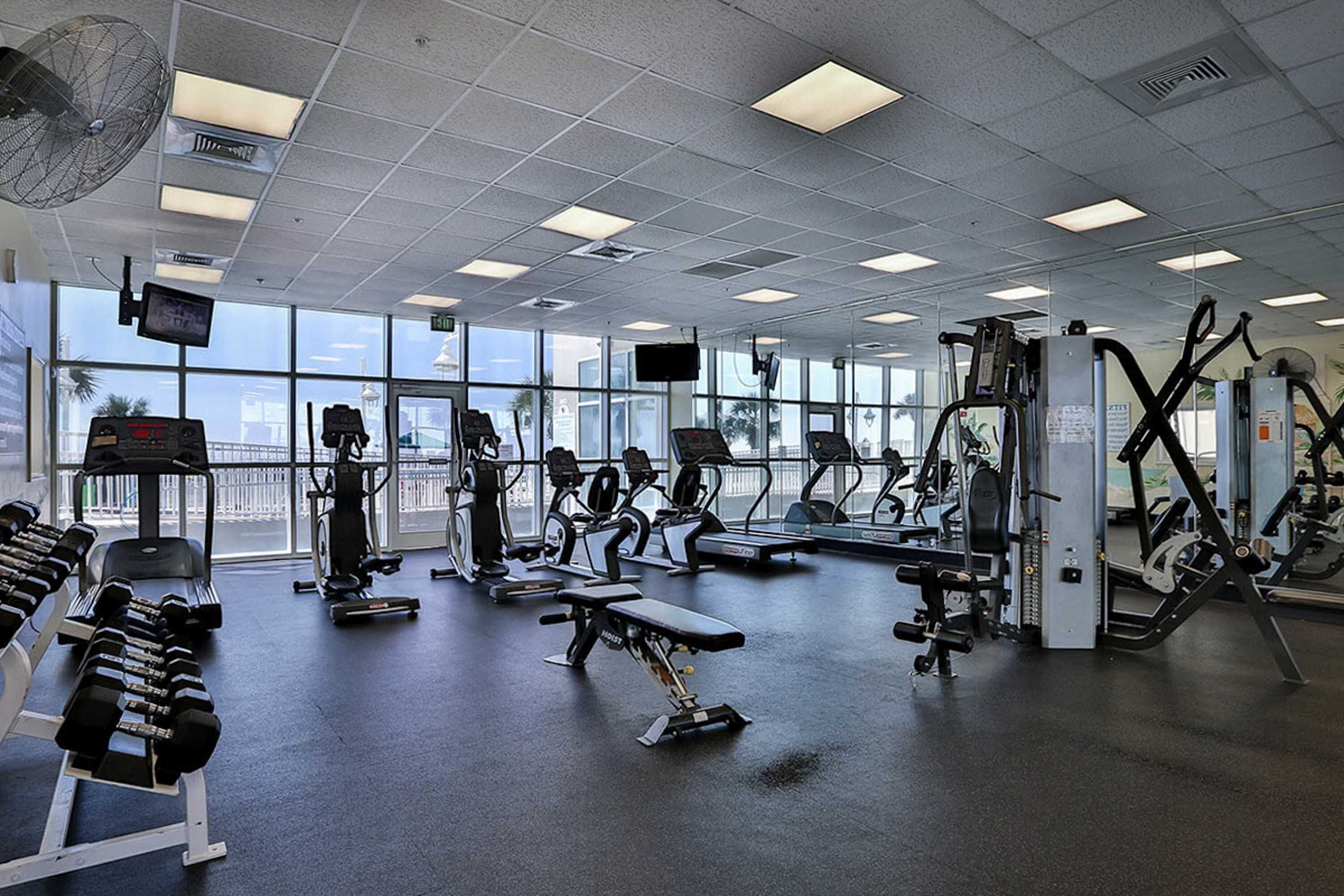 Ett gym med olika typer av träningsutrustning, stora fönster och utsikt över omgivningarna.
