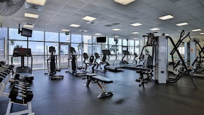 Uma academia com diversos equipamentos de exercício, janelas amplas e vista para o exterior.