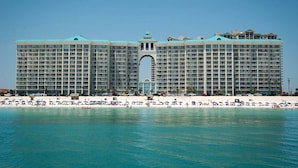 Um hotel grande com uma entrada em arco marcante, várias varandas e uma área de praia com guarda-sóis.