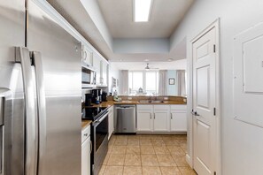 A modern kitchen with stainless steel appliances, white cabinets, and a large window providing natural light. - Newly updated picturesque third-floor Gulf-front condo on Okaloosa Island (Fort Walton Beach)