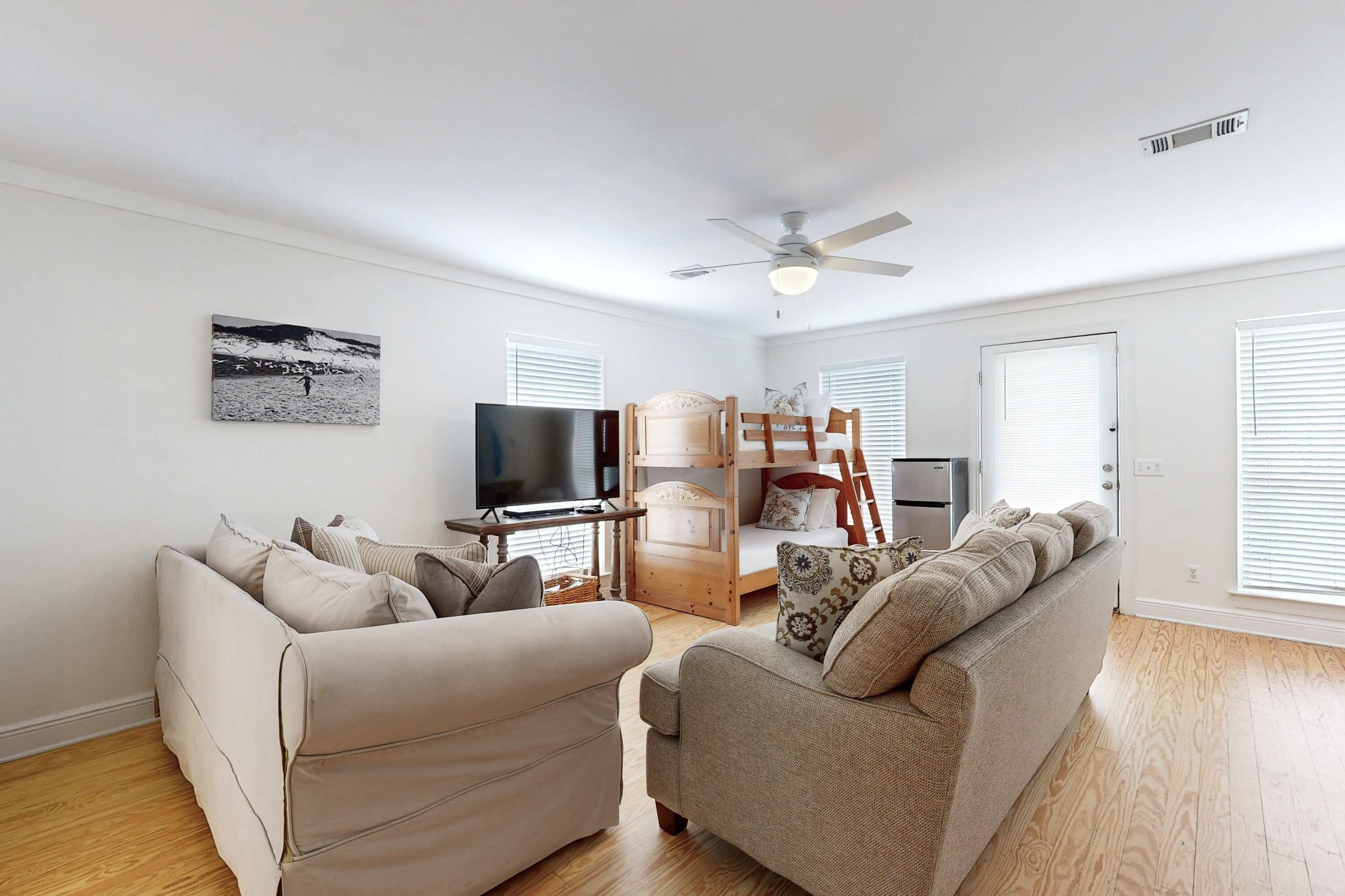 A spacious living room with a beige sofa, a wooden chair, a television, and a bunk bed.