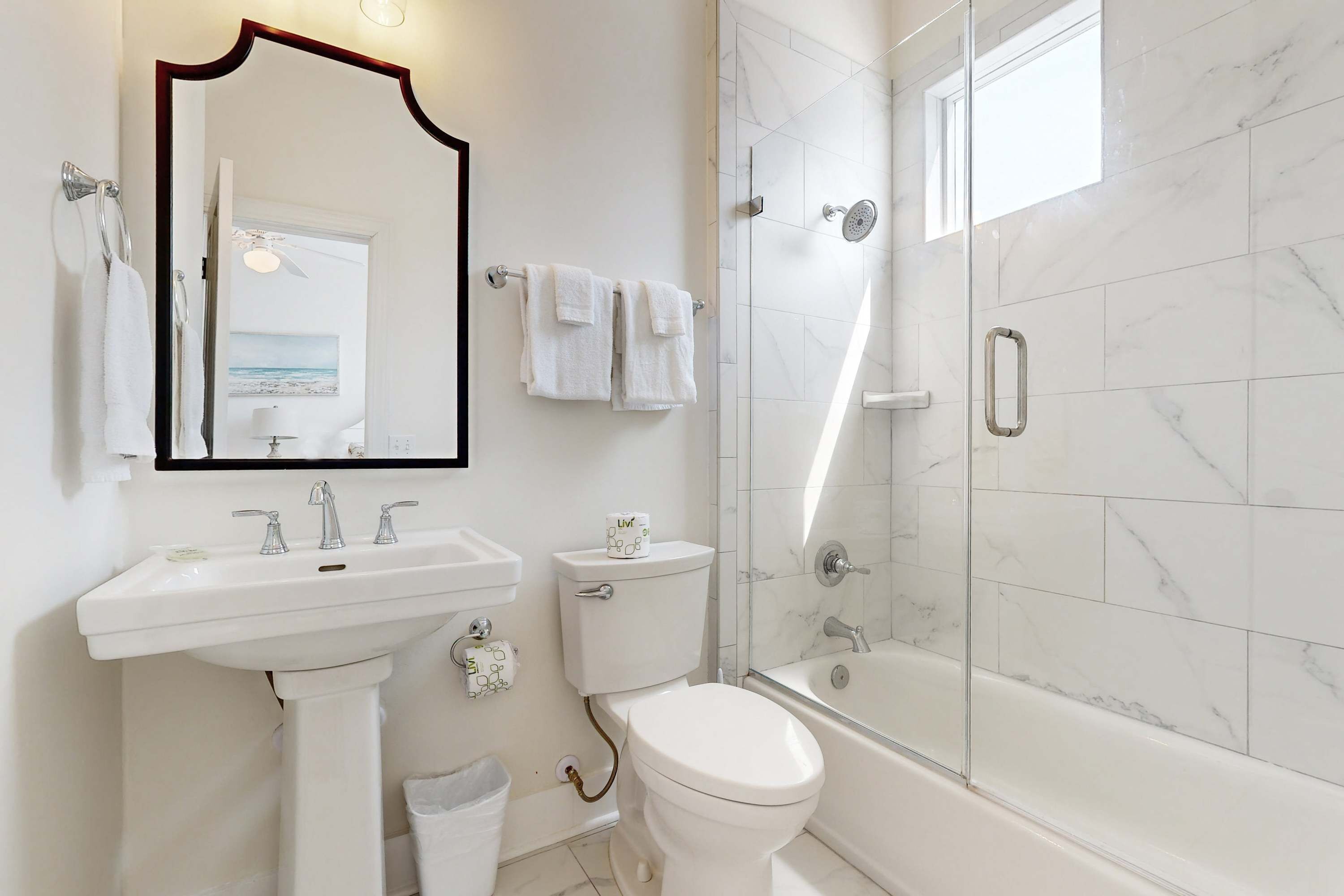 A modern bathroom with a white sink, toilet, and bathtub, marble tiles, and a large mirror.