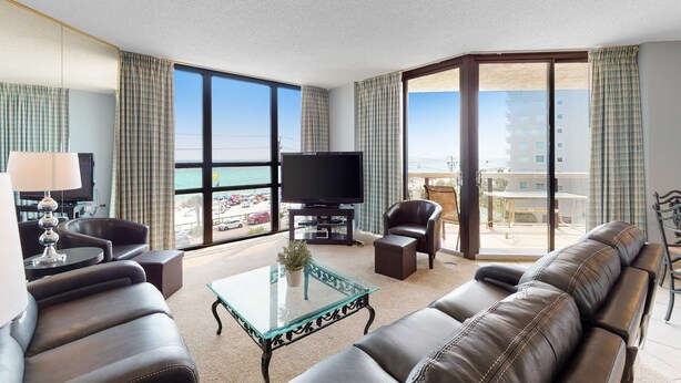 A modern hotel room with a large window, leather sofa, glass coffee table, and a flat-screen TV. - Beautiful beachside home w/central AC, internet, gulf views, shared pool/hot tub (Miramar Beach)