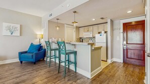 A modern kitchen with a central island, bar stools, and a blue armchair. - 3rd-floor Condo with pools, marina, tennis, large balcony, beach access (Miramar Beach)