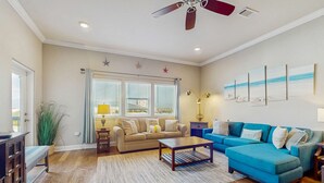 Ein Wohnzimmer mit einem beigefarbenen Sofa, einem blauen Ecksofa, einem Holztisch und einem Deckenventilator.