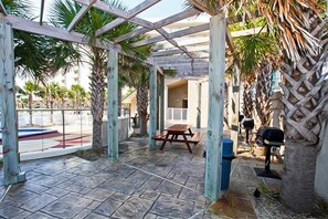 A covered outdoor area with stone flooring, wooden picnic tables, and palm trees. - 8th Floor Comfortable gulf view Condo, beach setup included, Near dining (Miramar Beach)