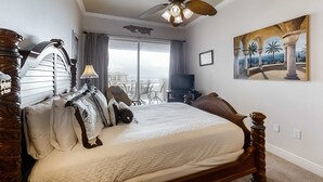 Un dormitorio con una cama grande, ventilador de techo, un cuadro y vistas al exterior.