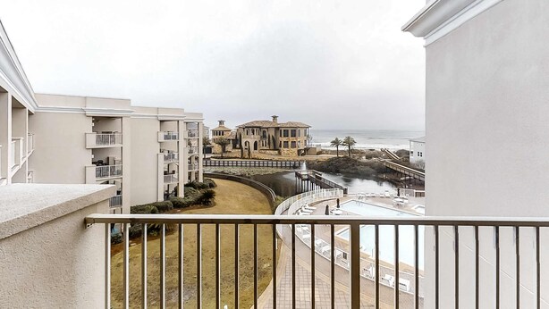 Un balcón con vistas a la costa, incluyendo un edificio grande con techo curvo y un puente que lleva a la playa.