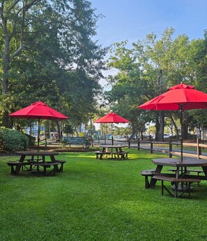 Un parque con mesas de picnic y sombrillas rojas.
