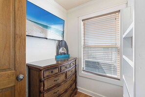 A room with a wooden dresser, a painting of a beach, and a window with blinds. - Beach Condo with Free WiFi, Washer/Dryer, Beach Service Now Included (Miramar Beach)